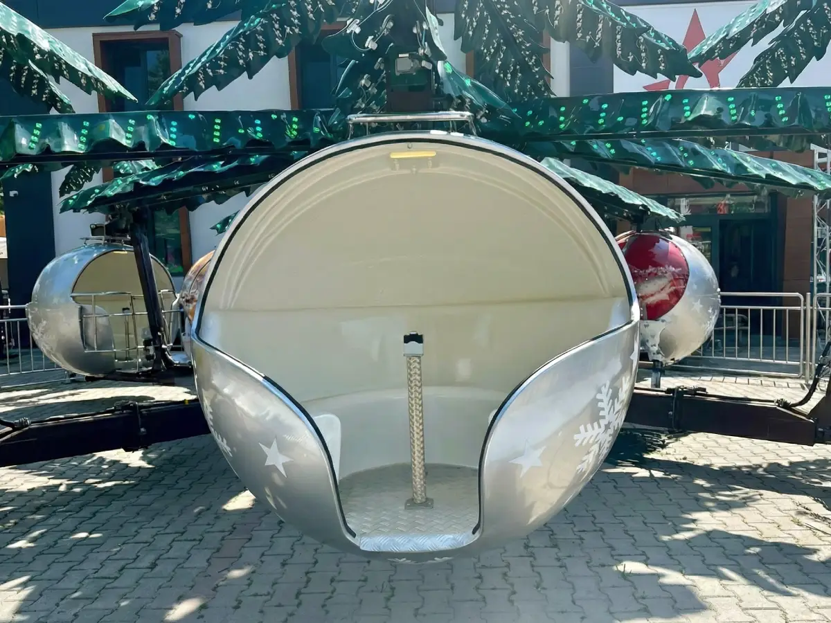 Primer plano de una cabina del carrusel Abeto Mágico con forma de bola de Navidad plateada, con el interior blanco y detalles de copos de nieve.